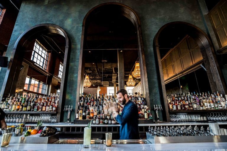 A bartender focused on mixing drinks, behind the bar of Death and Company. This bar lounge is located inside The Ramble Hotel.