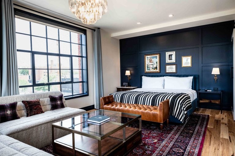 Perspective shot of the Salon Suite in the Ramble Hotel. Showing the bed, couch and table